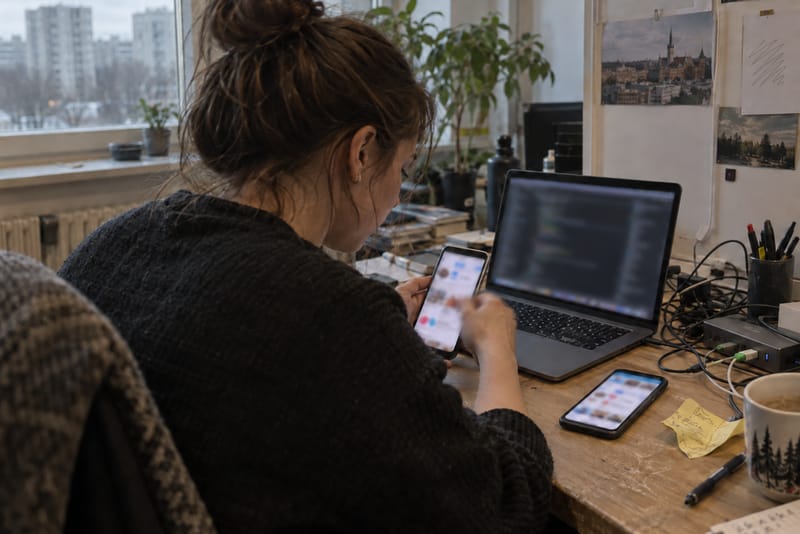 AI-generated image: a developer at a desk tries the same app on two different phones beside a laptop.